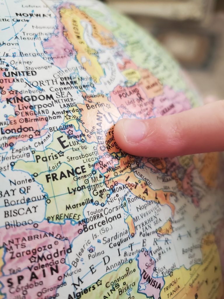 The image depicts a globe with a finger tipping on the European continent.