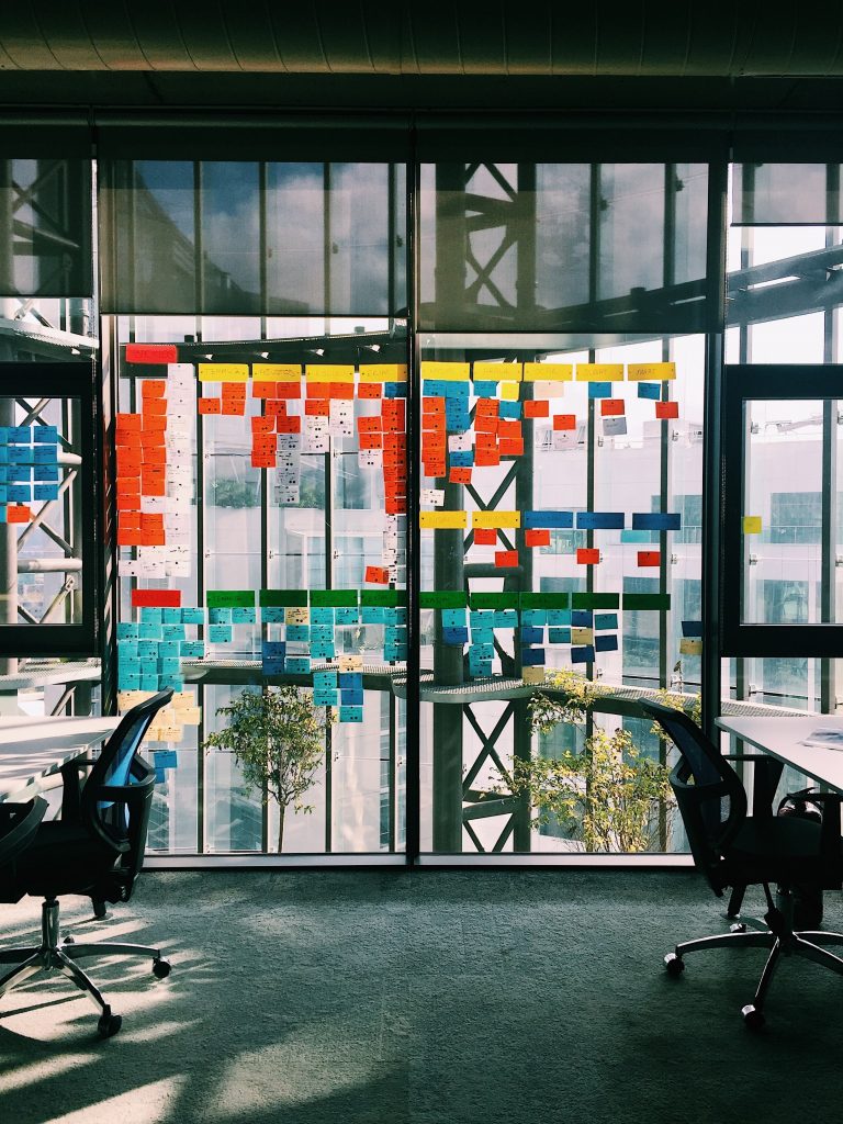 The image depicts an open working space with tables and a big window covered with plenty of colorful posts.