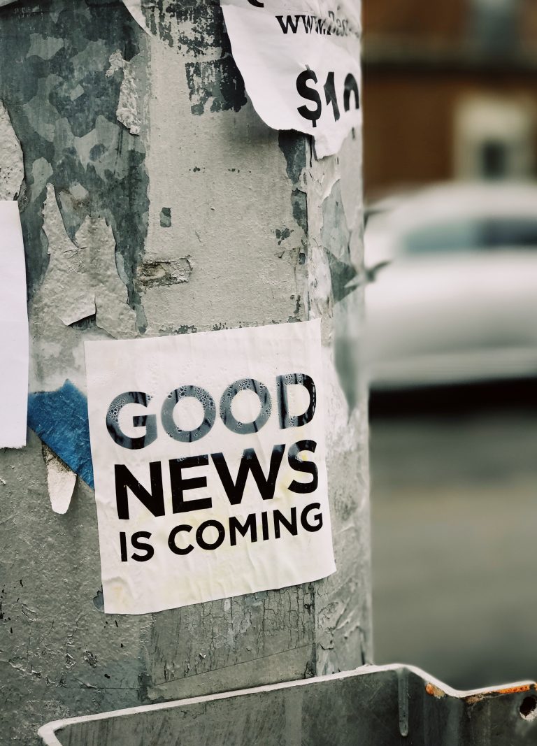 The image depicts a streetlight with a sticker “Good news is coming”.